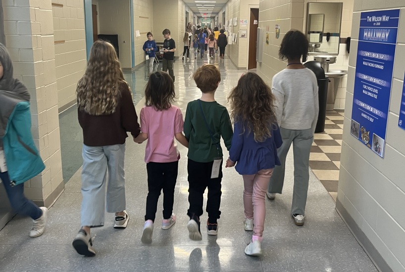 five students hold hands walking down the hallway